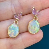 Hand holding Tura Sugden Opal + Sapphire Earrings: oval opals with pink sapphire accents on top.